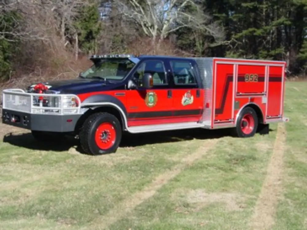 Exterior view of small fire truck showing cab, body compartments, and wheel/tire area.