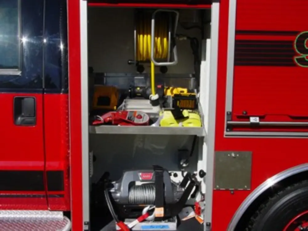 Exterior view of small fire truck showing cab, body compartments, and wheel/tire area.