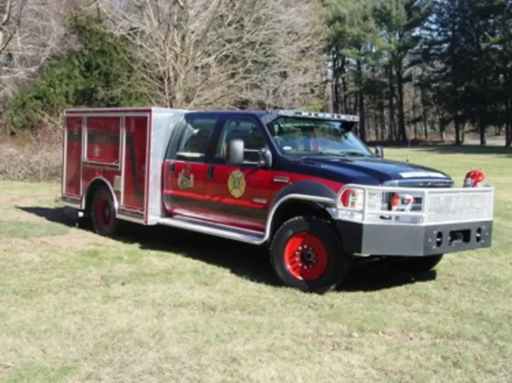 Exterior view of small fire truck showing cab, body compartments, and wheel/tire area.