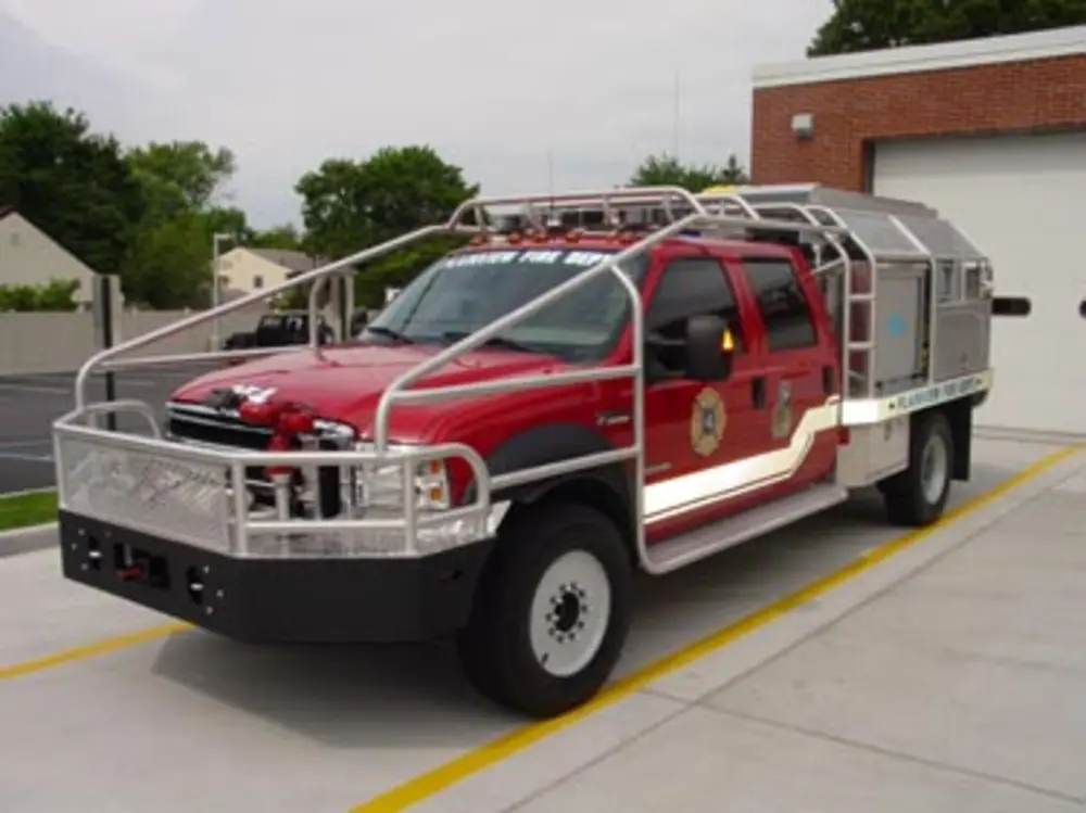 Exterior view of small fire truck showing cab, body compartments, and wheel/tire area.