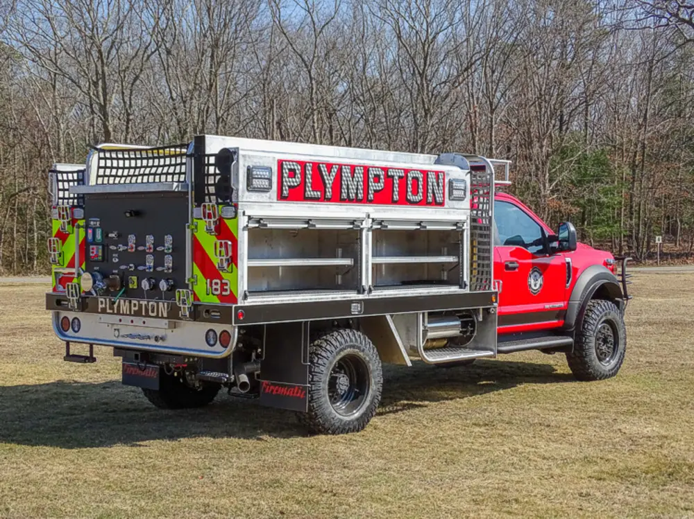 Exterior view of small fire truck showing cab, body compartments, and wheel/tire area.
