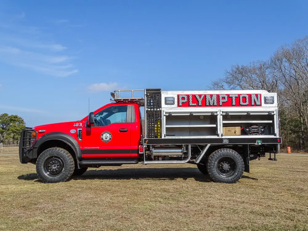 Exterior view of small fire truck showing cab, body compartments, and wheel/tire area.