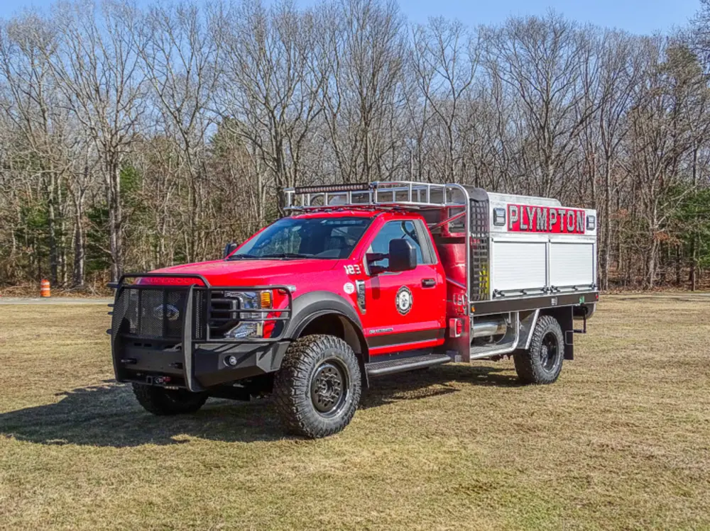 Exterior view of small fire truck showing cab, body compartments, and wheel/tire area.