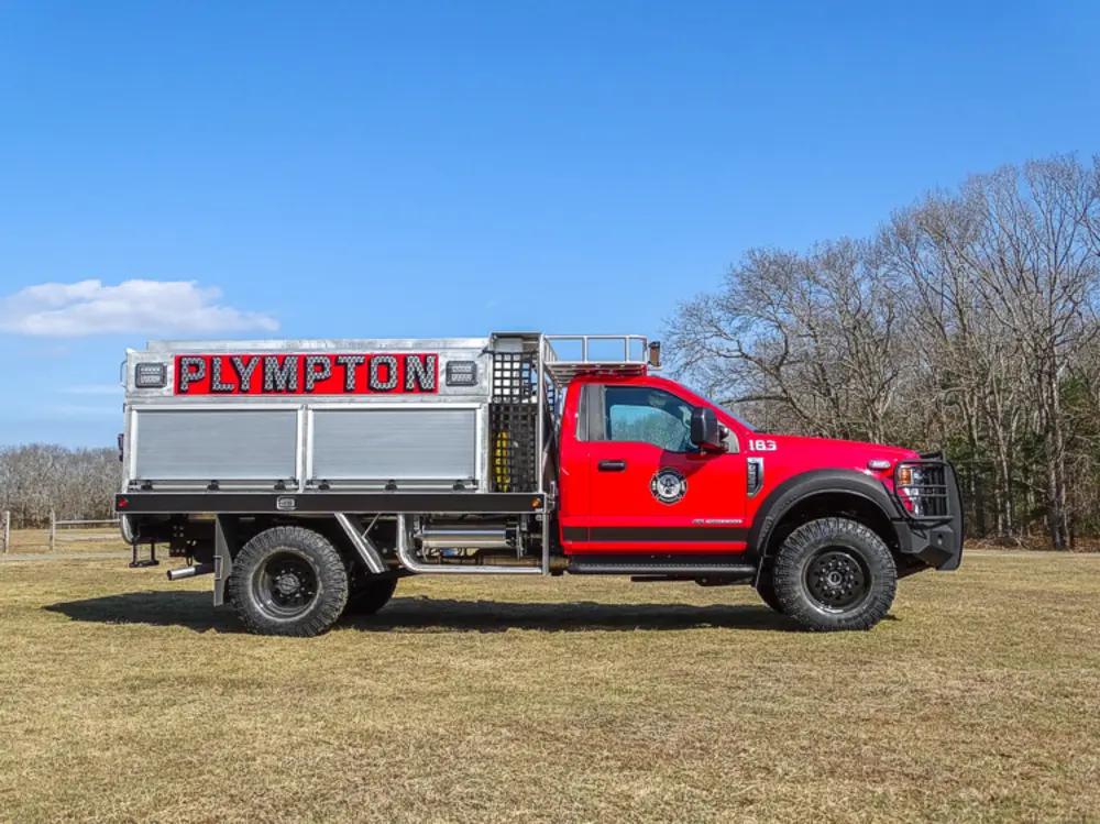 Exterior view of small fire truck showing cab, body compartments, and wheel/tire area.