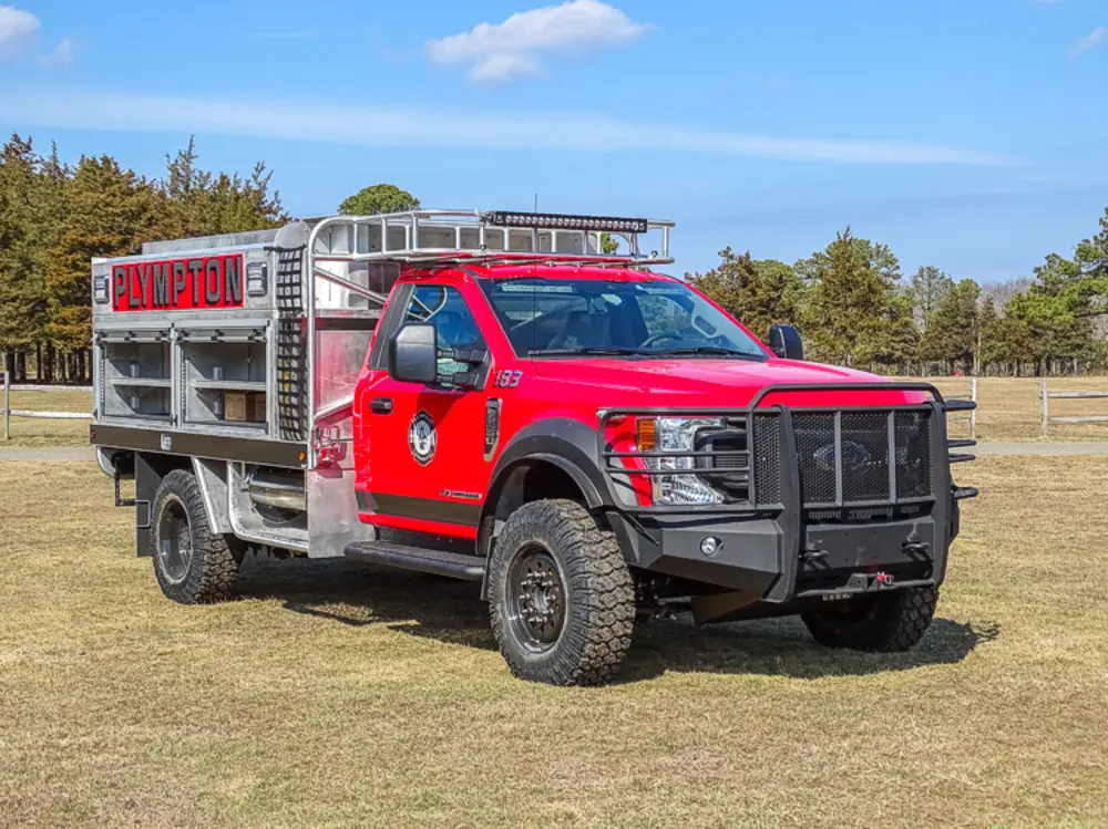 Exterior view of small fire truck showing cab, body compartments, and wheel/tire area.