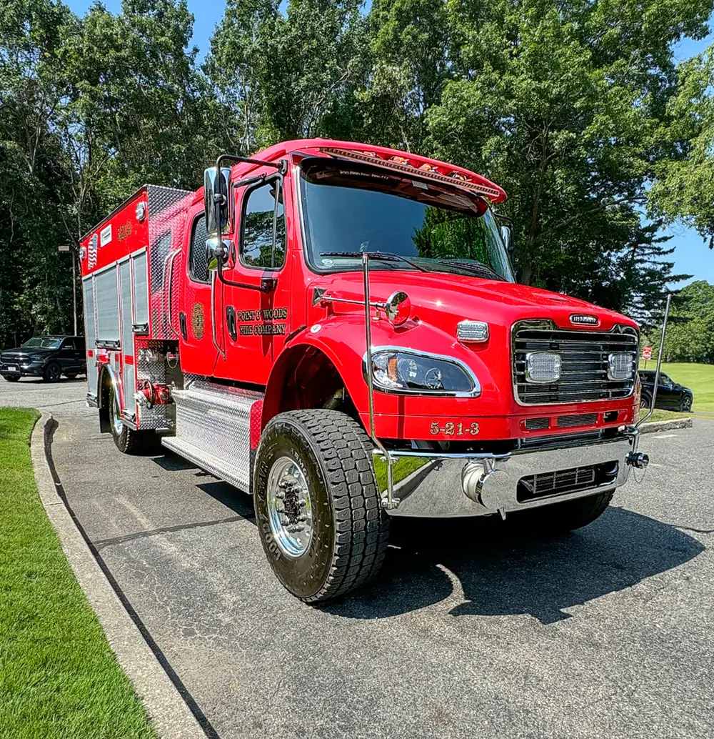 Exterior view of small fire truck showing cab, body compartments, and wheel/tire area.
