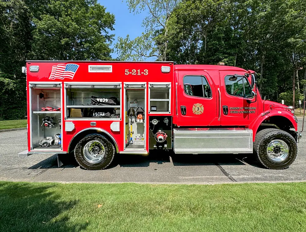 Exterior view of small fire truck showing cab, body compartments, and wheel/tire area.