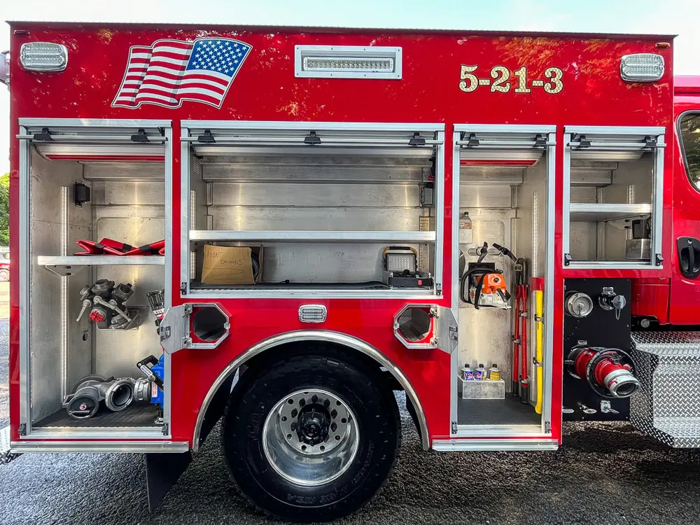 Exterior view of small fire truck showing cab, body compartments, and wheel/tire area.