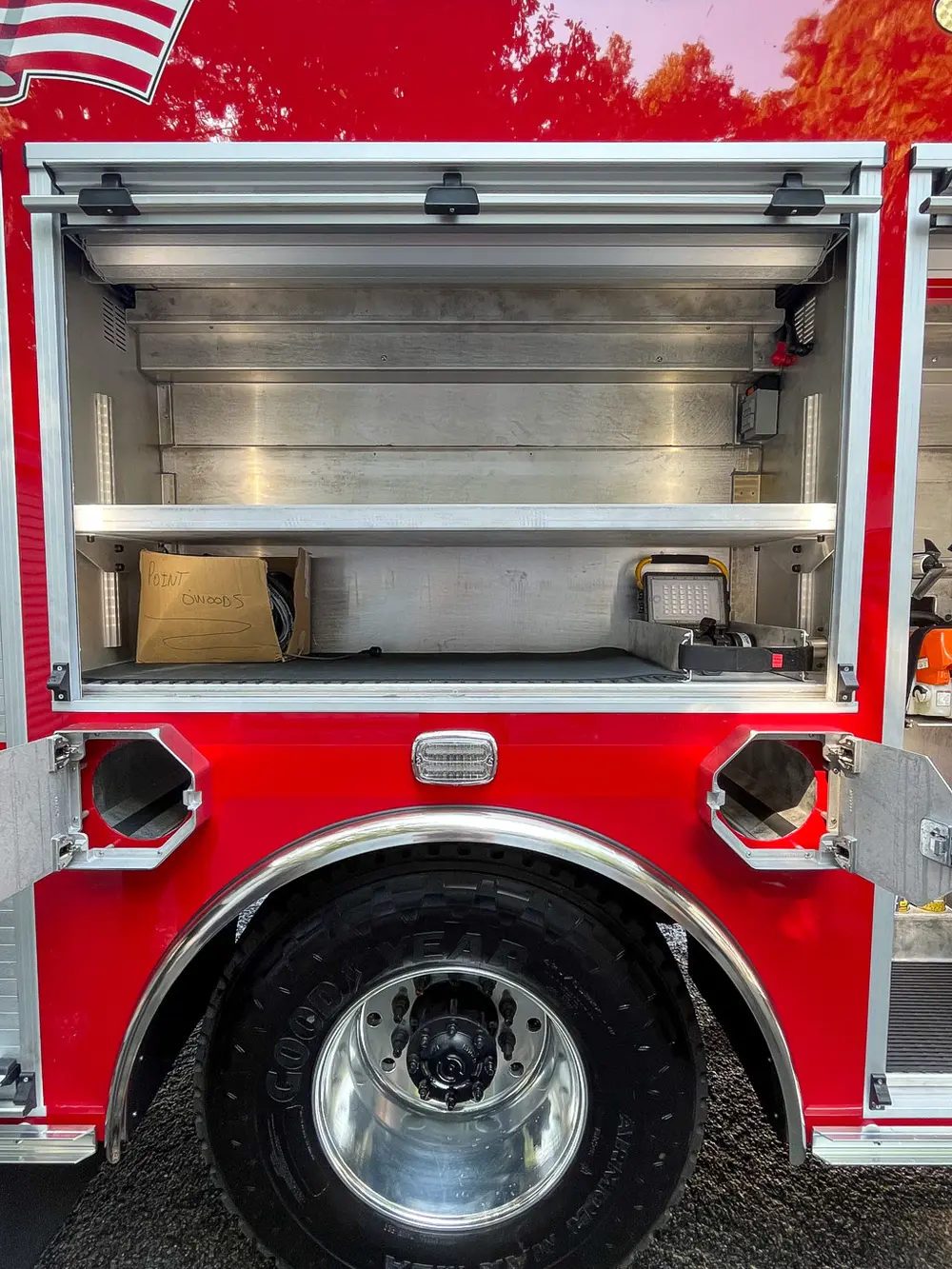 Exterior view of small fire truck showing cab, body compartments, and wheel/tire area.