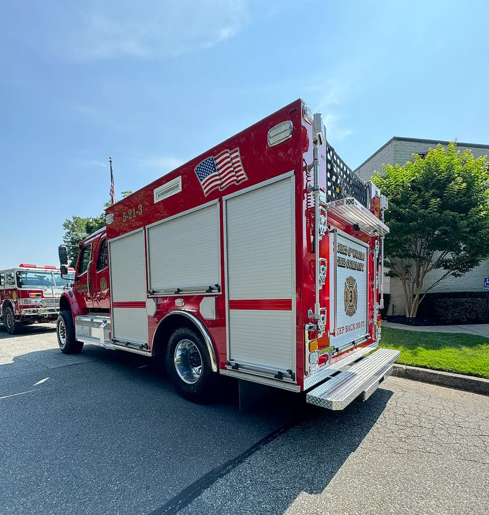 Exterior view of small fire truck showing cab, body compartments, and wheel/tire area.