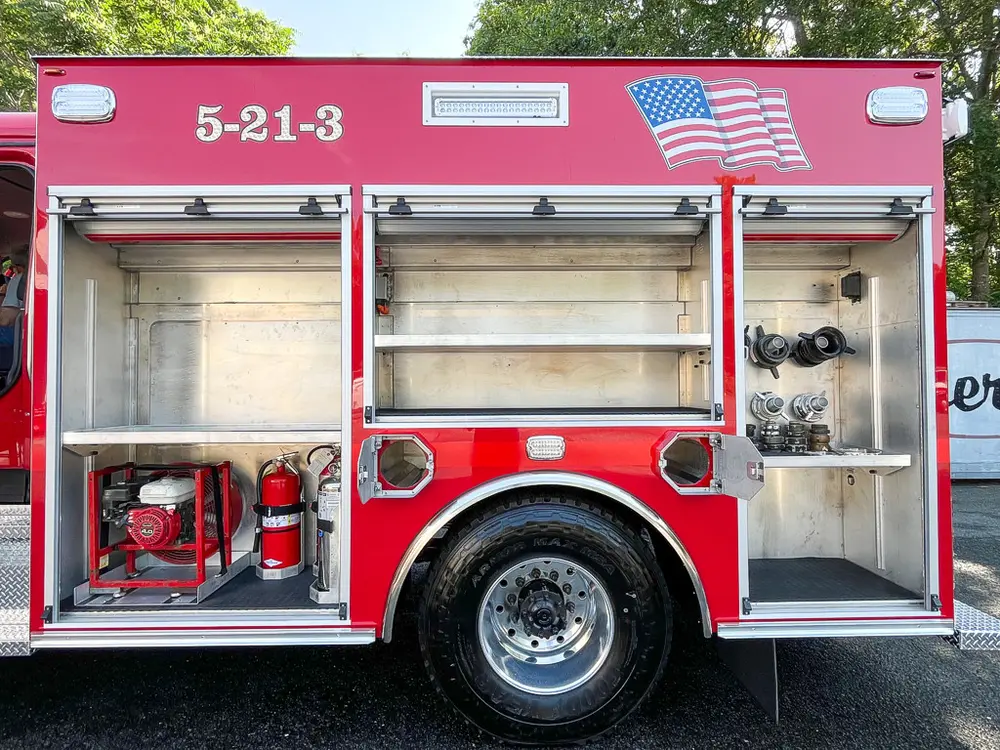 Exterior view of small fire truck showing cab, body compartments, and wheel/tire area.