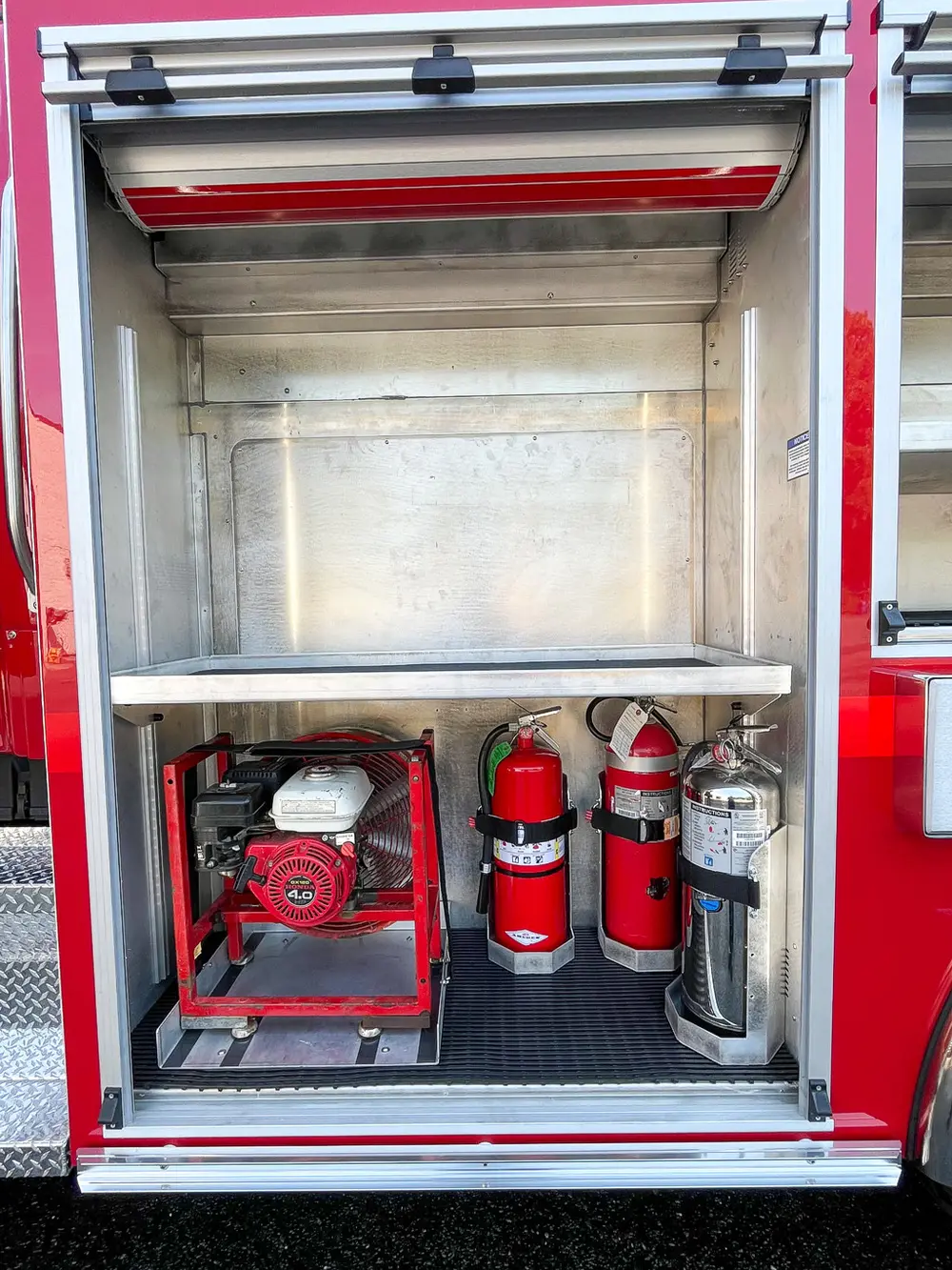 Exterior view of small fire truck showing cab, body compartments, and wheel/tire area.