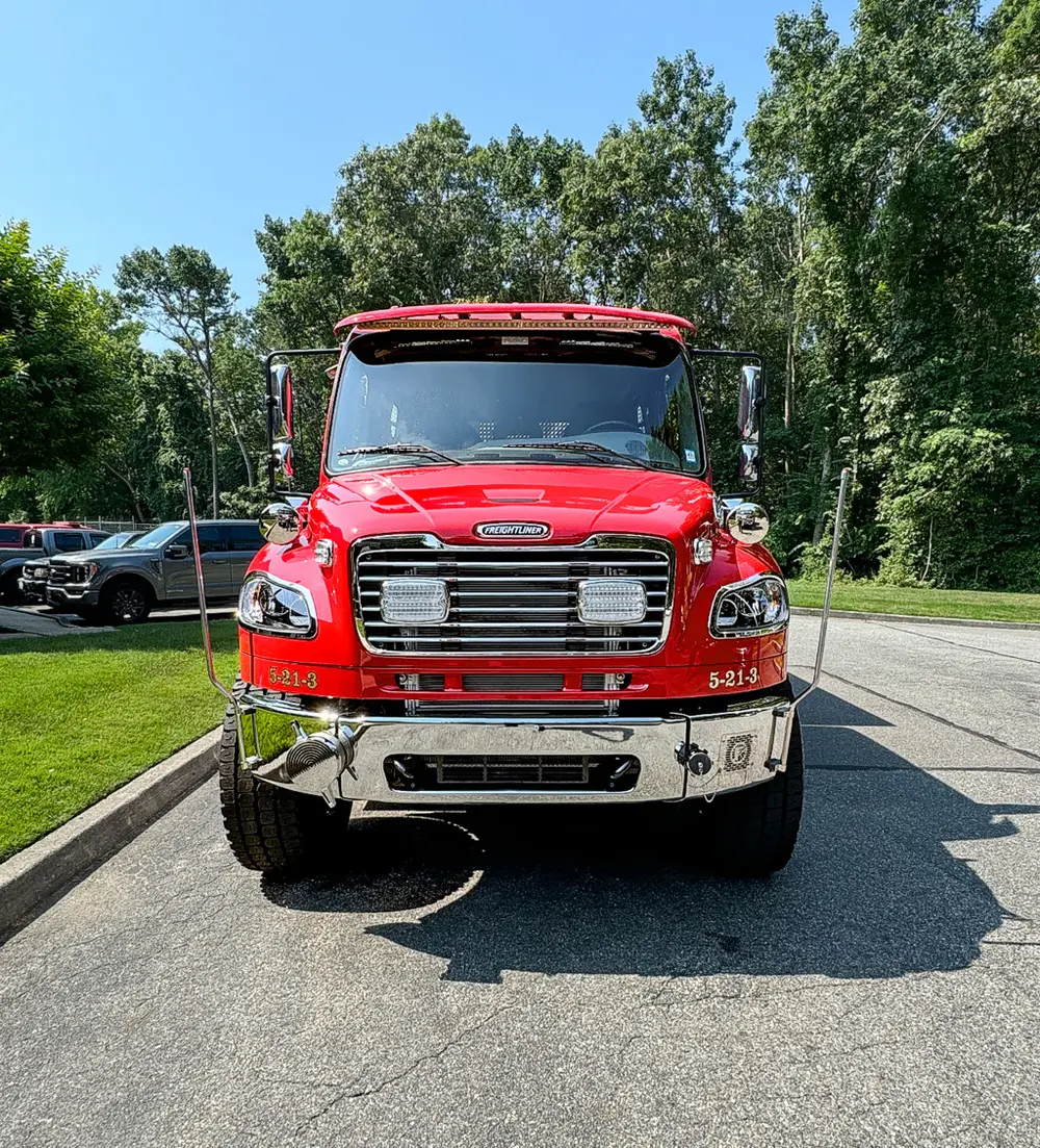 Exterior view of small fire truck showing cab, body compartments, and wheel/tire area.