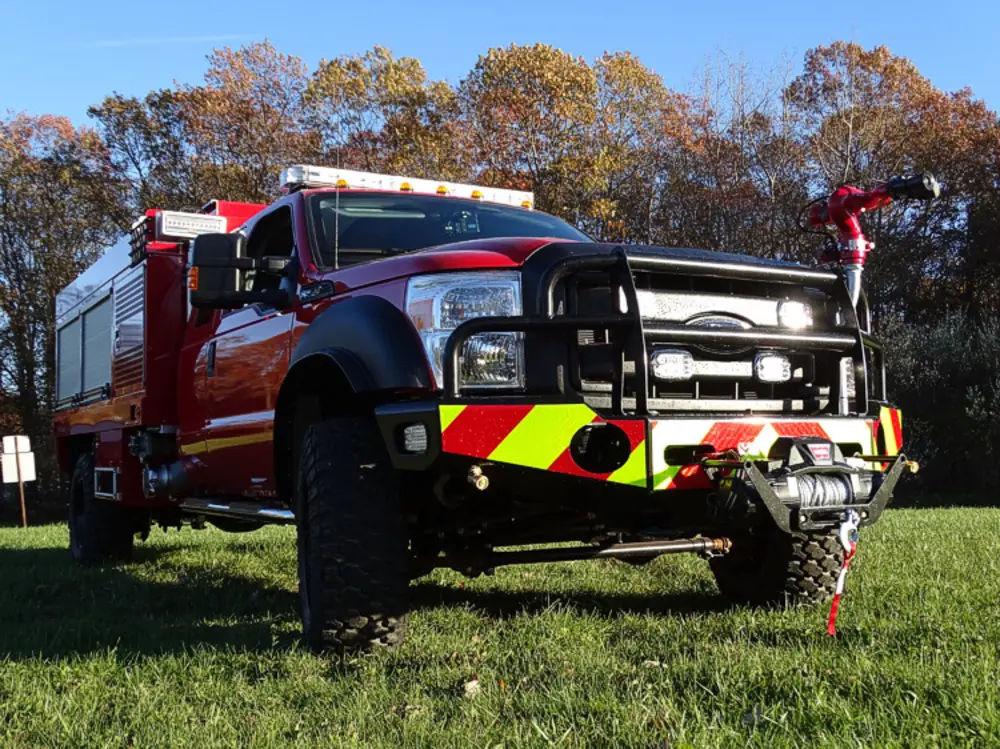 Exterior view of small fire truck showing cab, body compartments, and wheel/tire area.