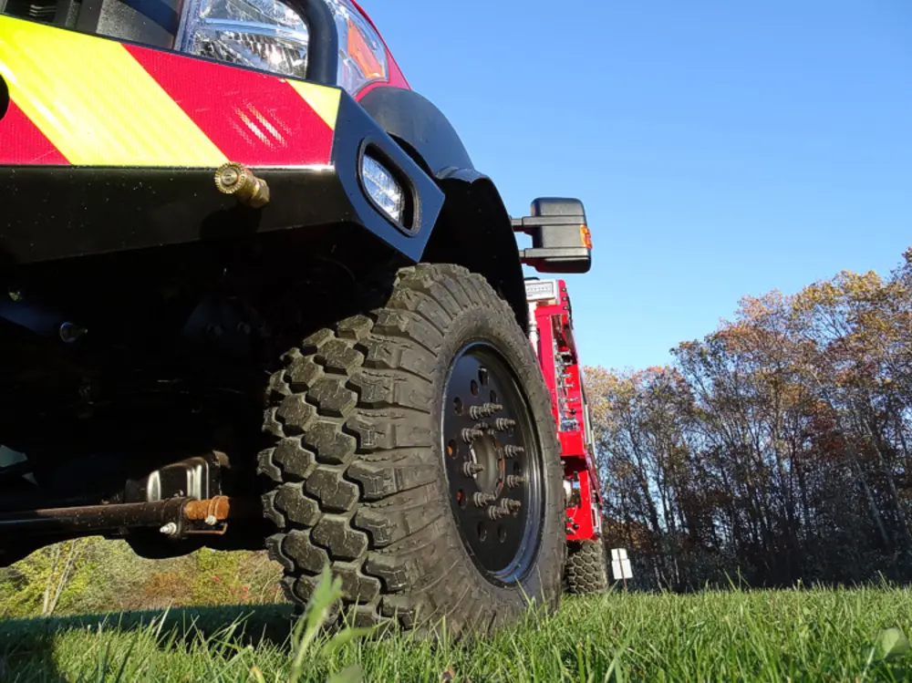 Exterior view of small fire truck showing cab, body compartments, and wheel/tire area.