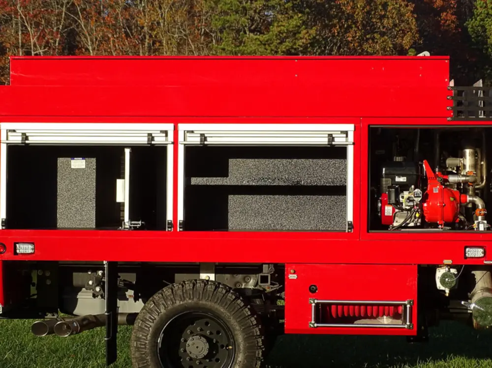 Exterior view of small fire truck showing cab, body compartments, and wheel/tire area.