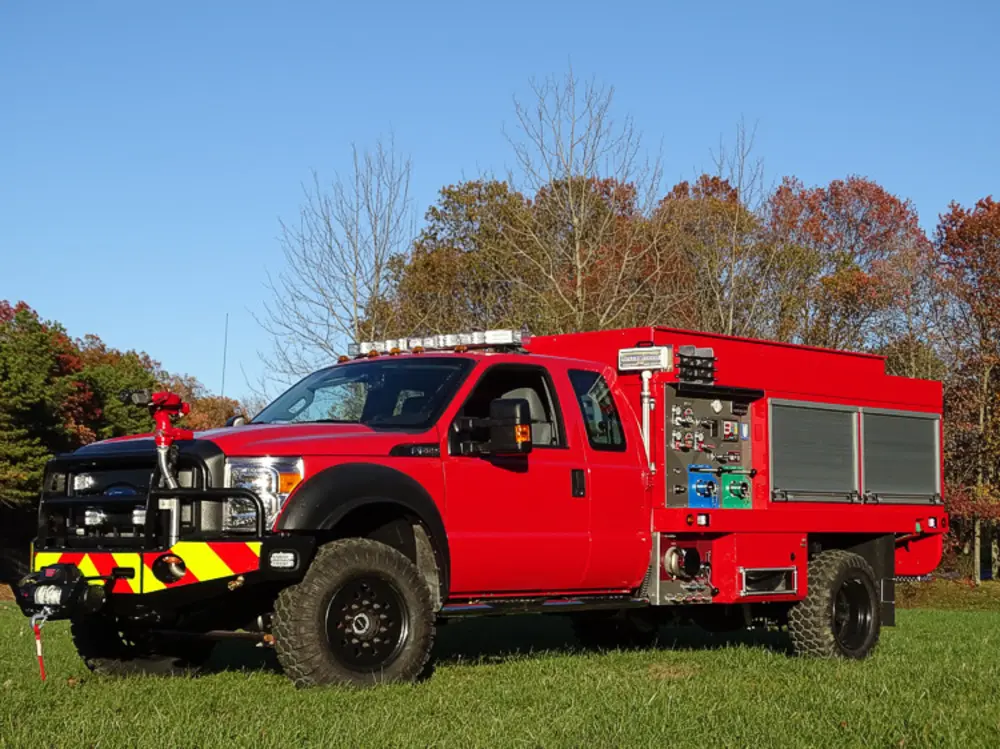 Exterior view of small fire truck showing cab, body compartments, and wheel/tire area.