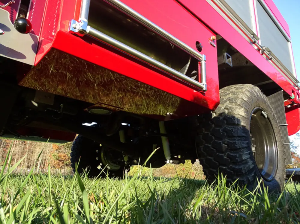 Exterior view of small fire truck showing cab, body compartments, and wheel/tire area.