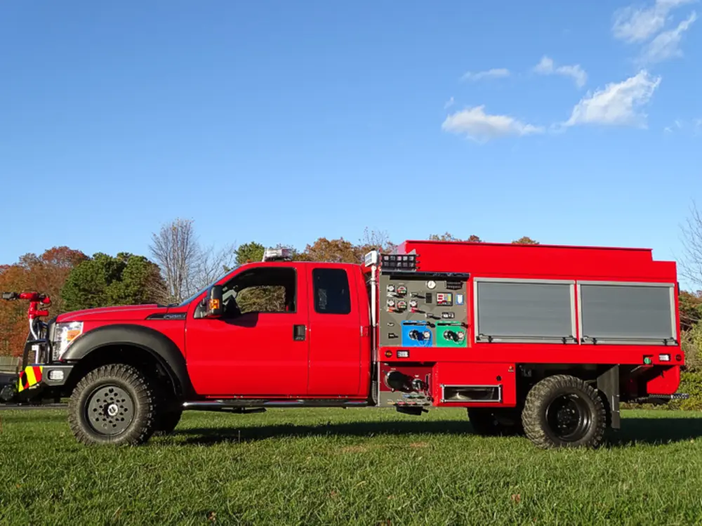 Exterior view of small fire truck showing cab, body compartments, and wheel/tire area.