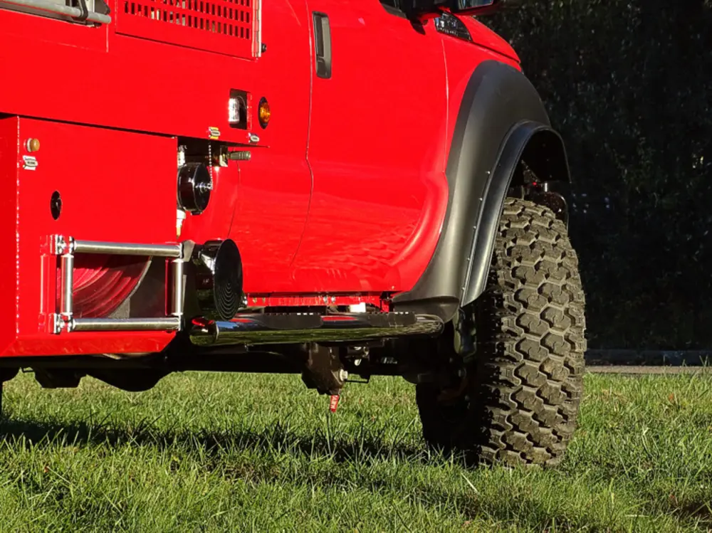 Exterior view of small fire truck showing cab, body compartments, and wheel/tire area.