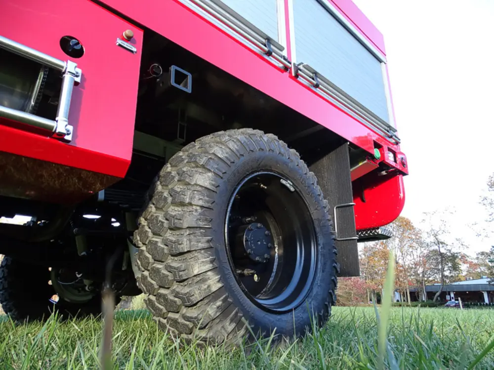 Exterior view of small fire truck showing cab, body compartments, and wheel/tire area.
