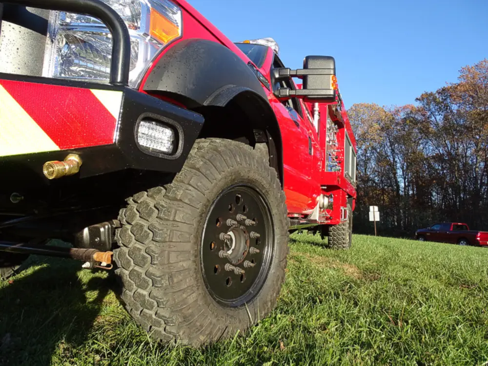 Exterior view of small fire truck showing cab, body compartments, and wheel/tire area.
