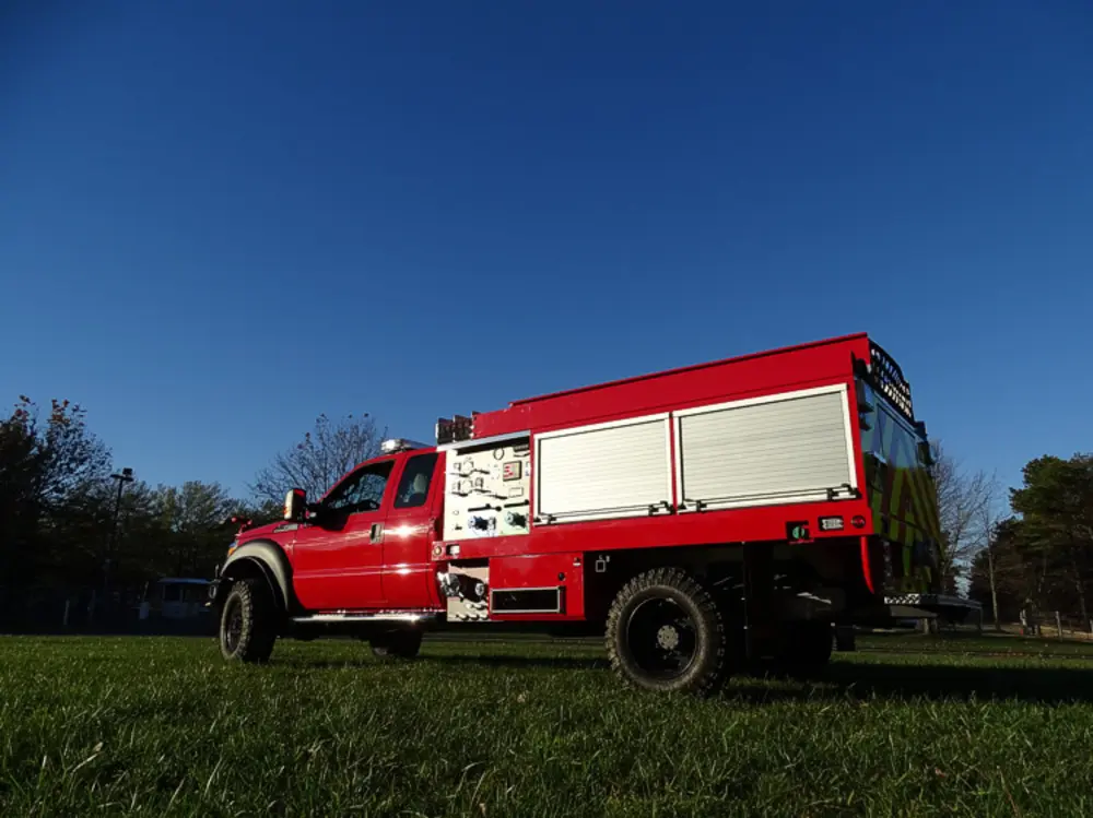 Exterior view of small fire truck showing cab, body compartments, and wheel/tire area.