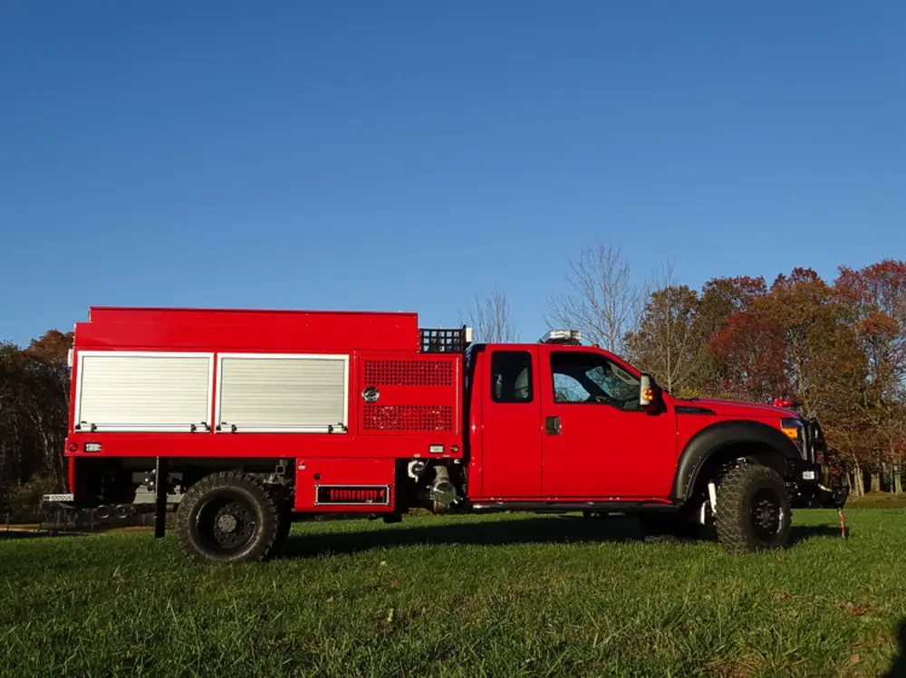 Exterior view of small fire truck showing cab, body compartments, and wheel/tire area.