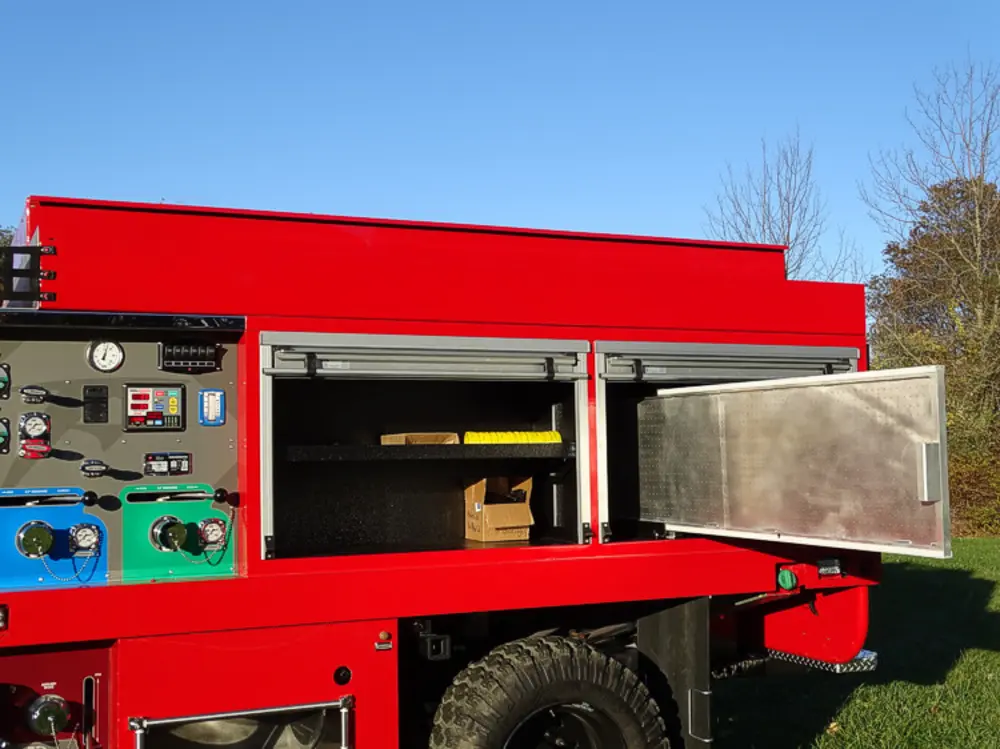 Exterior view of small fire truck showing cab, body compartments, and wheel/tire area.