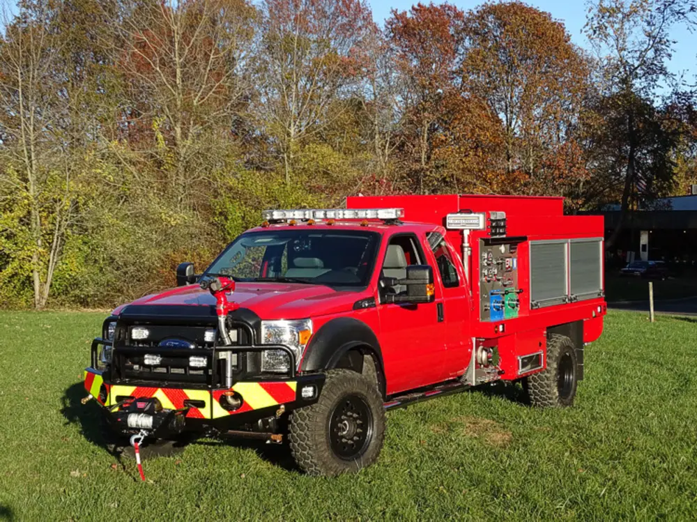 Exterior view of small fire truck showing cab, body compartments, and wheel/tire area.