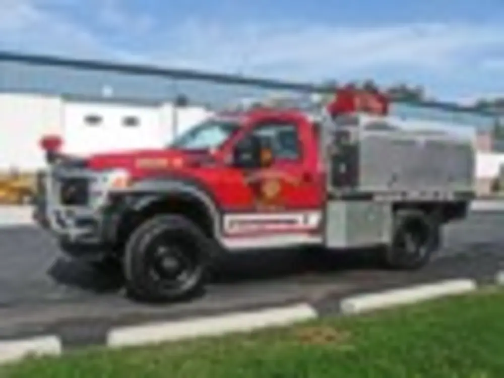 Exterior view of small fire truck showing cab, body compartments, and wheel/tire area.
