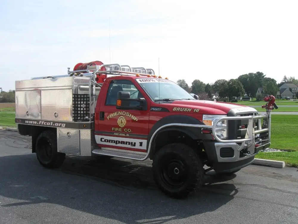 Exterior view of small fire truck showing cab, body compartments, and wheel/tire area.
