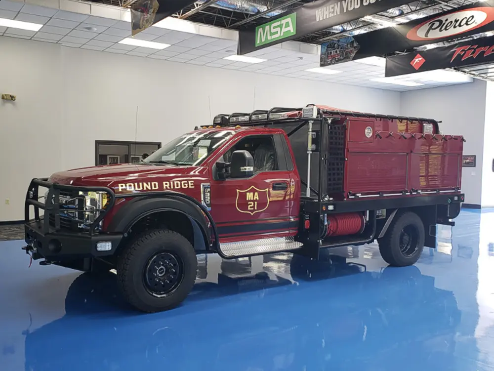 Exterior view of small fire truck showing cab, body compartments, and wheel/tire area.