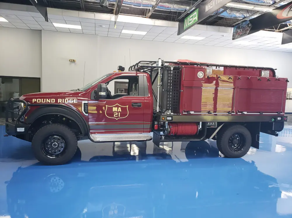 Exterior view of small fire truck showing cab, body compartments, and wheel/tire area.