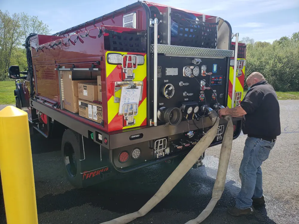 Exterior view of small fire truck showing cab, body compartments, and wheel/tire area.