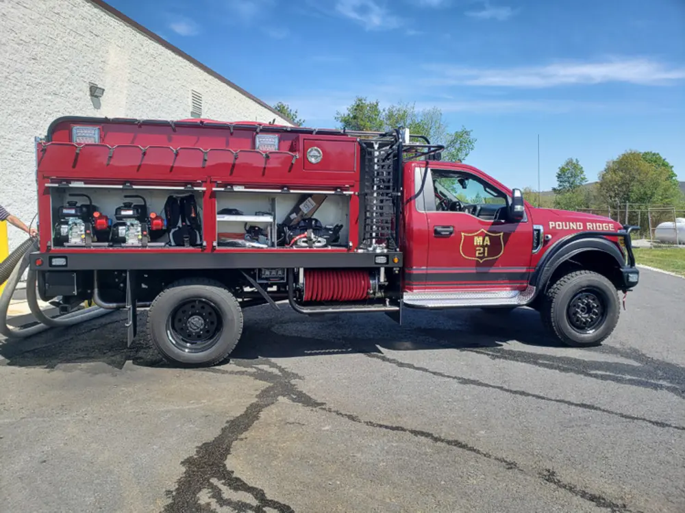 Exterior view of small fire truck showing cab, body compartments, and wheel/tire area.