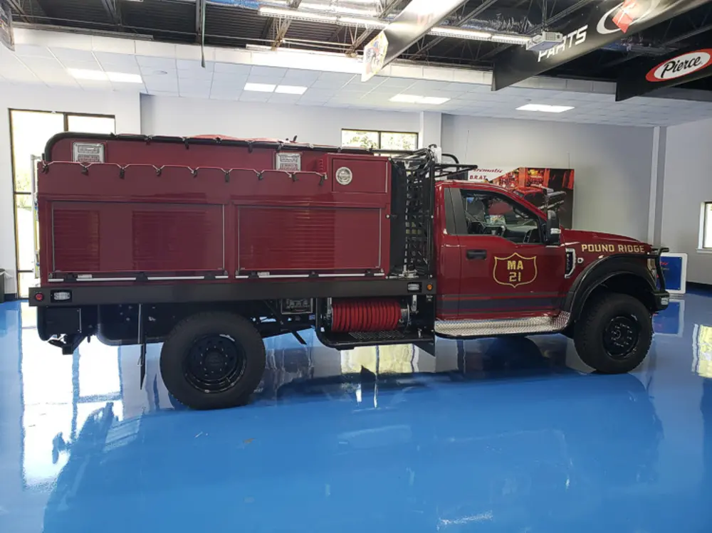 Exterior view of small fire truck showing cab, body compartments, and wheel/tire area.