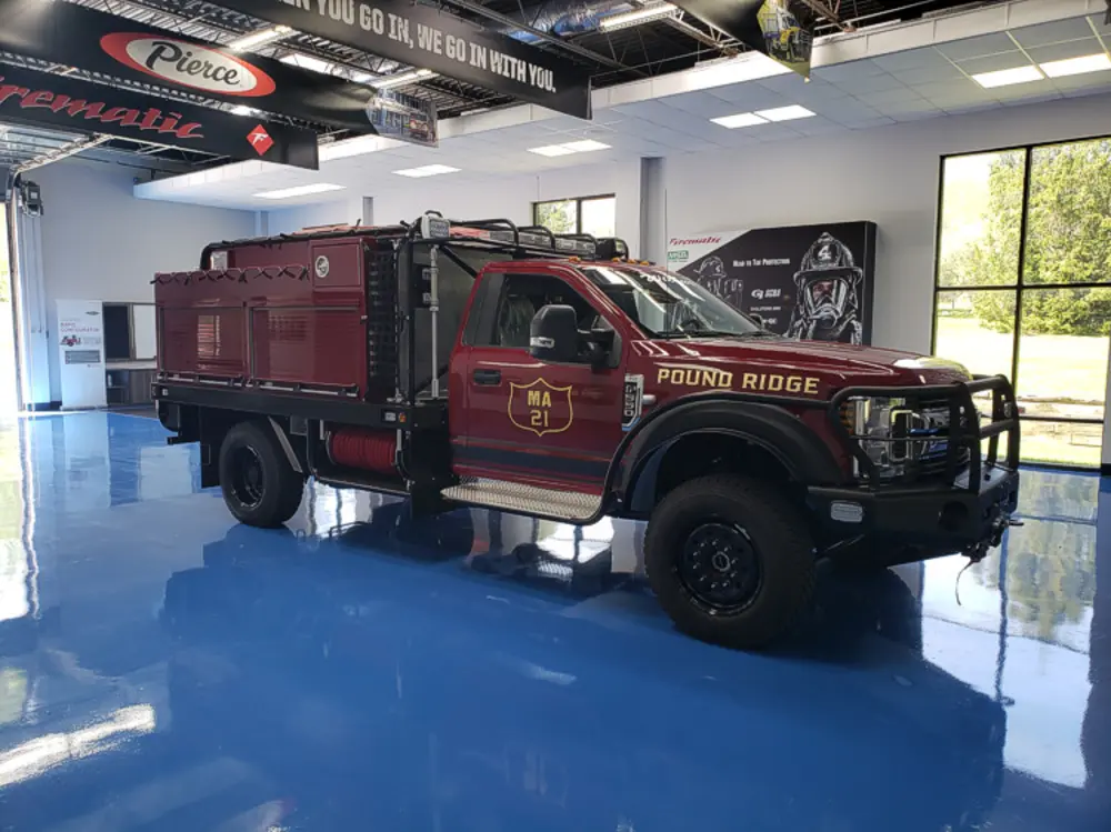 Exterior view of small fire truck showing cab, body compartments, and wheel/tire area.