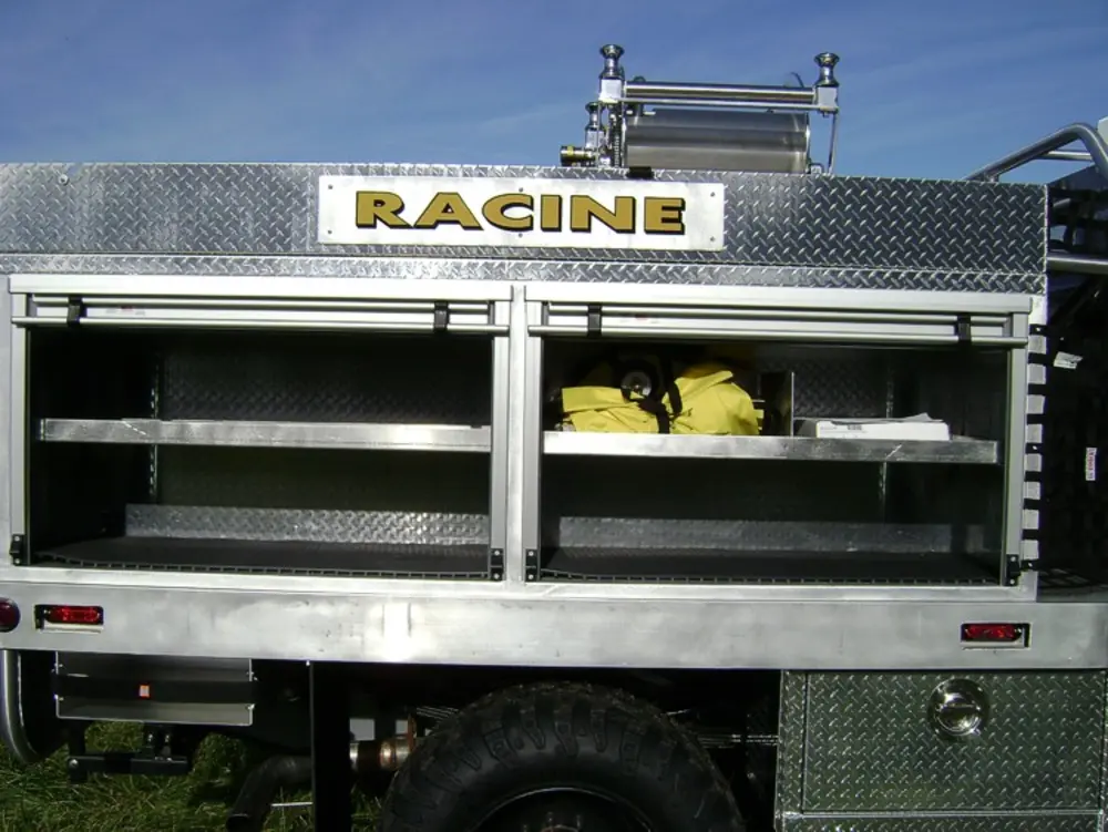 Exterior view of small fire truck showing cab, body compartments, and wheel/tire area.