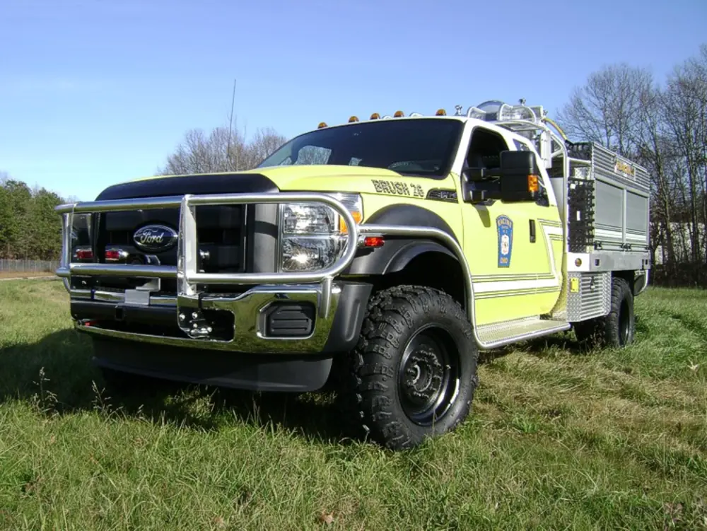 Exterior view of small fire truck showing cab, body compartments, and wheel/tire area.