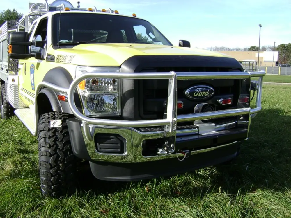 Exterior view of small fire truck showing cab, body compartments, and wheel/tire area.