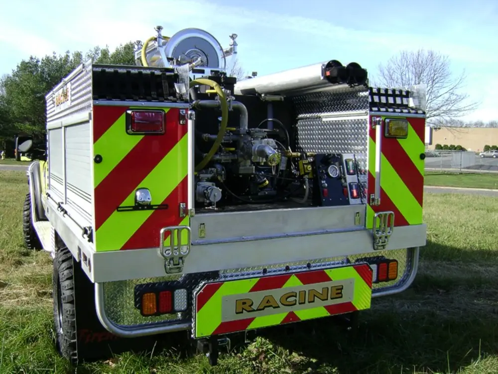 Exterior view of small fire truck showing cab, body compartments, and wheel/tire area.