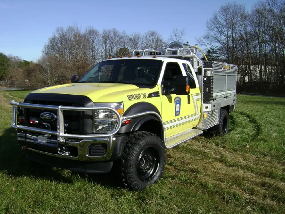 Exterior view of small fire truck showing cab, body compartments, and wheel/tire area.