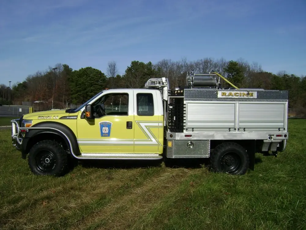 Exterior view of small fire truck showing cab, body compartments, and wheel/tire area.