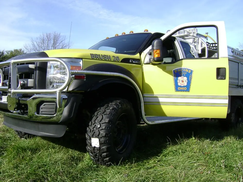 Exterior view of small fire truck showing cab, body compartments, and wheel/tire area.