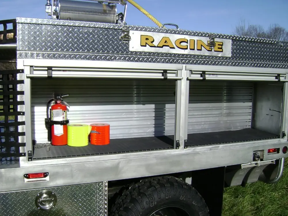 Exterior view of small fire truck showing cab, body compartments, and wheel/tire area.