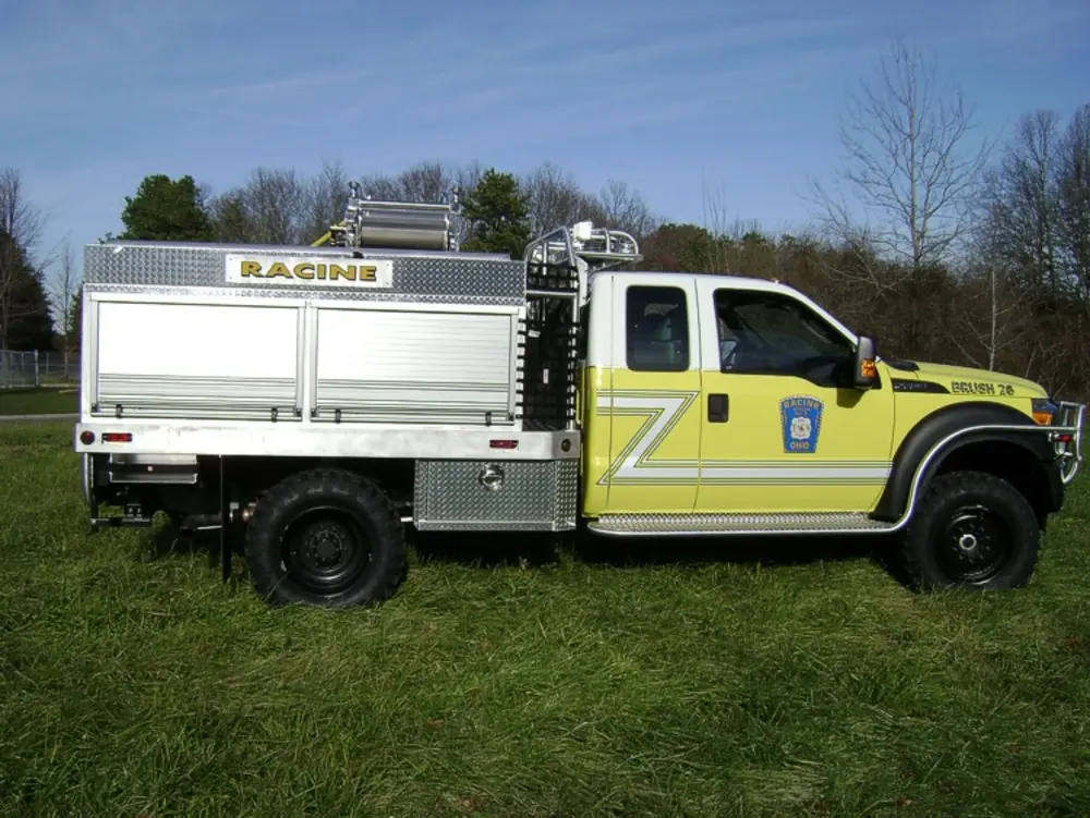 Exterior view of small fire truck showing cab, body compartments, and wheel/tire area.