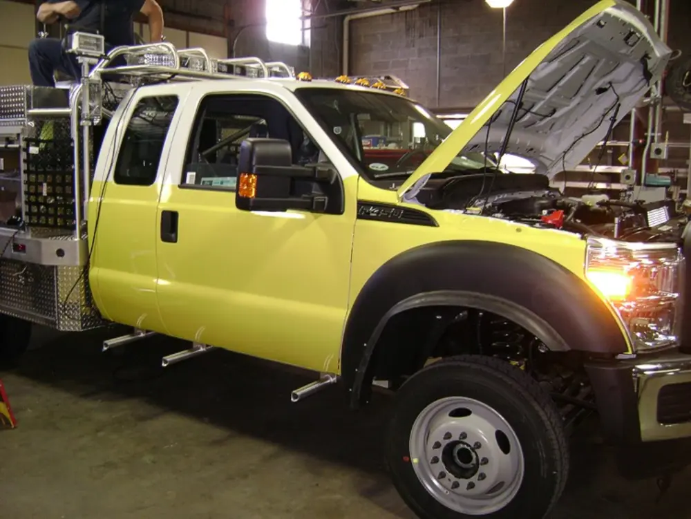 Exterior view of small fire truck showing cab, body compartments, and wheel/tire area.