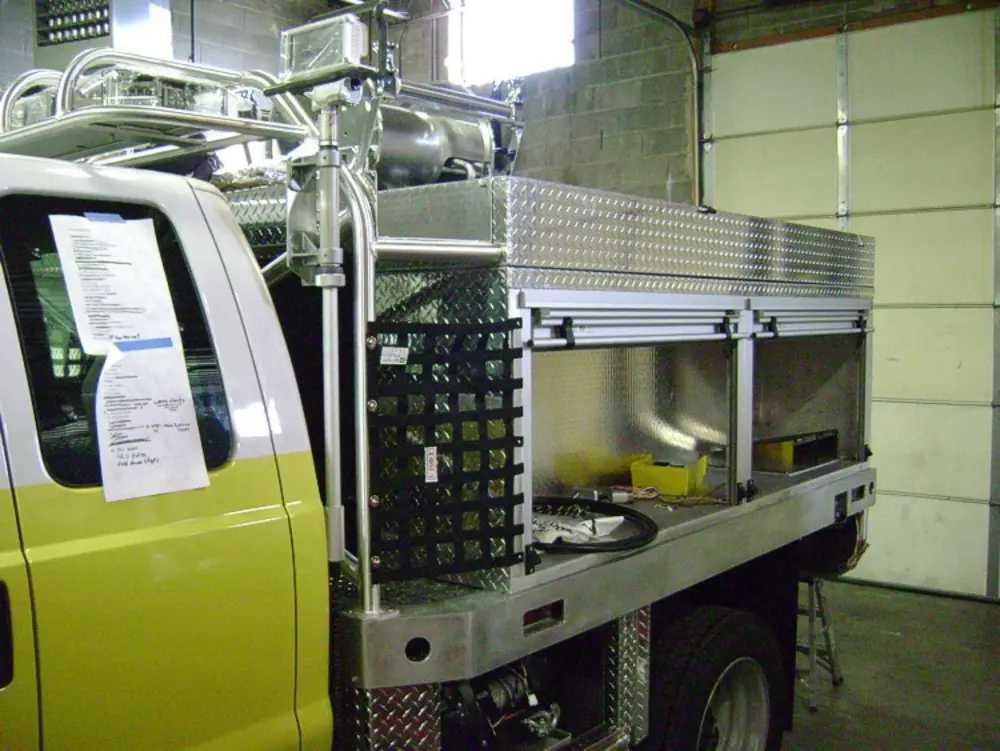 Exterior view of small fire truck showing cab, body compartments, and wheel/tire area.