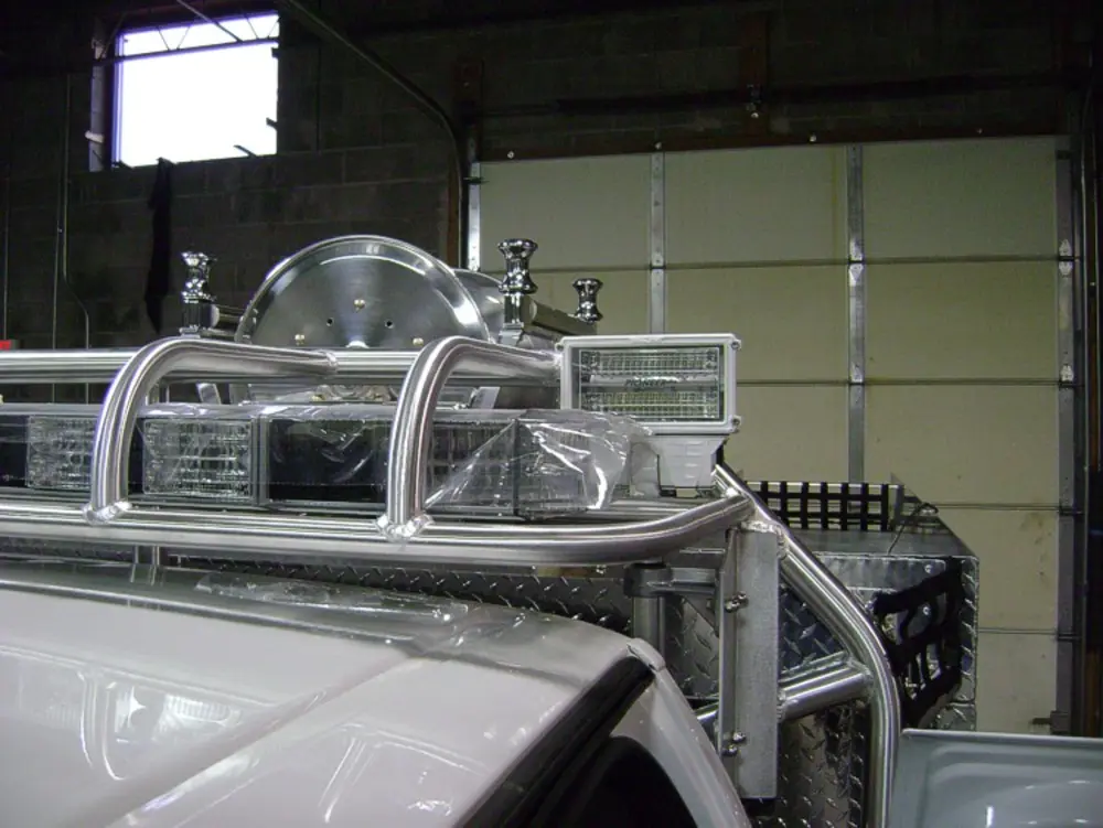 Exterior view of small fire truck showing cab, body compartments, and wheel/tire area.